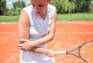 eine Frau auf dem Tennisplatz, die sich den schmerzenden Ellenbogen hält
