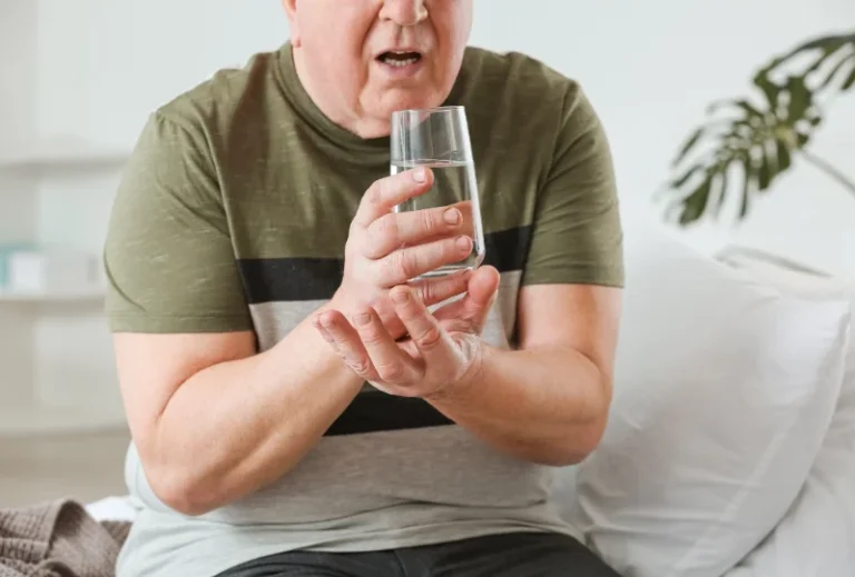 Älterer Mann mit Zittern in der Hand hält ein Glas Wasser und zeigt Anzeichen von Parkinson.